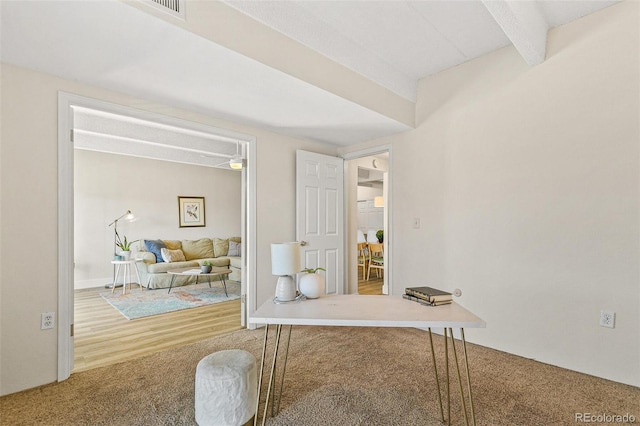 carpeted office space featuring beam ceiling