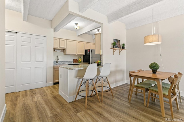 kitchen with a kitchen breakfast bar, beam ceiling, light brown cabinets, and stainless steel refrigerator