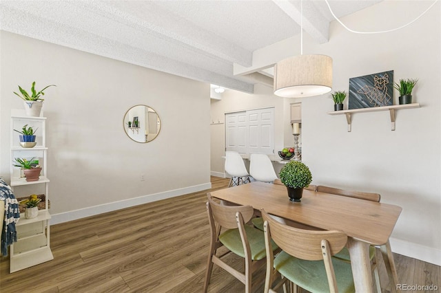 dining area featuring beam ceiling, dark hardwood / wood-style flooring, and a textured ceiling