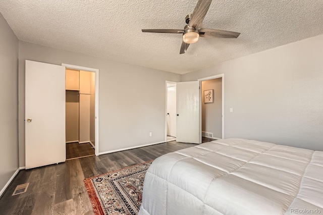 bedroom with wood finished floors, a textured ceiling, a walk in closet, a ceiling fan, and a closet