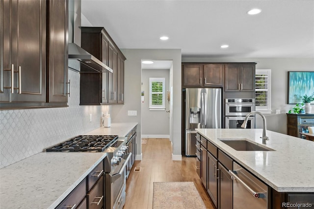 5608 Raintree Dr, Parker, CO 80134 - kitchen featuring appliances with stainless steel finishes, wall chimney range hood, light wood-type flooring, dark brown cabinetry, and recessed lighting