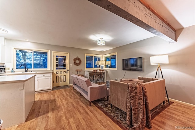 living room featuring beam ceiling, baseboards, and light wood finished floors