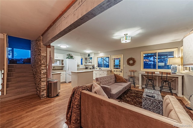 living area featuring light wood-style flooring, stairs, baseboards, and beam ceiling