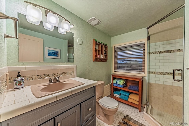 full bathroom featuring a textured wall, toilet, vanity, decorative backsplash, and a stall shower