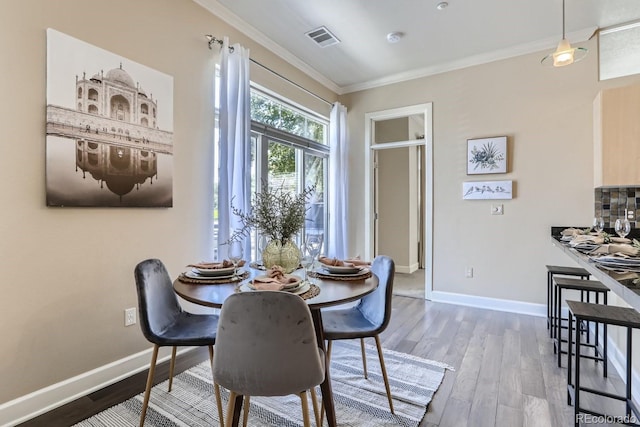 dining space with baseboards, wood finished floors, visible vents, and ornamental molding