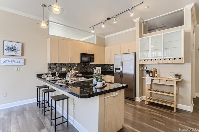 kitchen featuring light brown cabinets, a sink, stainless steel refrigerator with ice dispenser, black microwave, and a kitchen bar