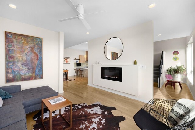 living room with light wood-style flooring, recessed lighting, a ceiling fan, stairway, and a glass covered fireplace