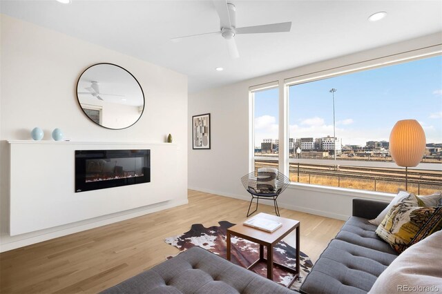 living area with recessed lighting, a city view, a ceiling fan, light wood-style floors, and a glass covered fireplace