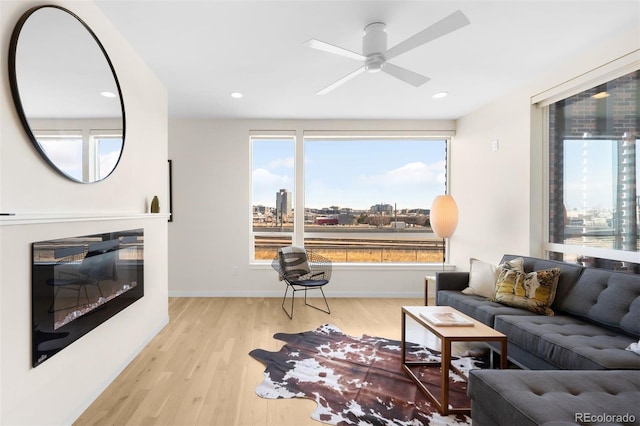 living room with baseboards, a ceiling fan, a glass covered fireplace, wood finished floors, and a city view