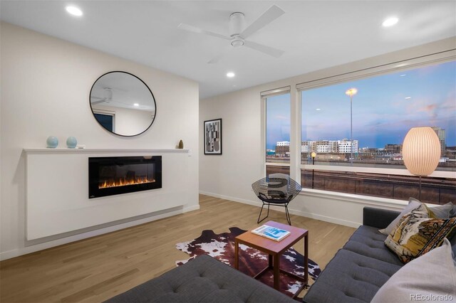 living area featuring baseboards, a ceiling fan, a glass covered fireplace, wood finished floors, and recessed lighting