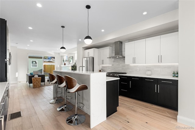 kitchen with a breakfast bar area, light countertops, high end refrigerator, dark cabinetry, and wall chimney exhaust hood