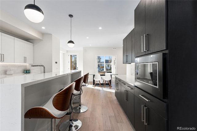 kitchen with a breakfast bar, light wood-style flooring, decorative light fixtures, tasteful backsplash, and built in microwave