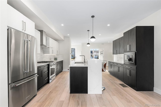 kitchen with wall chimney range hood, light countertops, premium appliances, light wood-style floors, and a sink