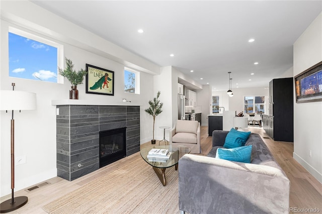 living area with light wood finished floors, visible vents, baseboards, a tiled fireplace, and recessed lighting