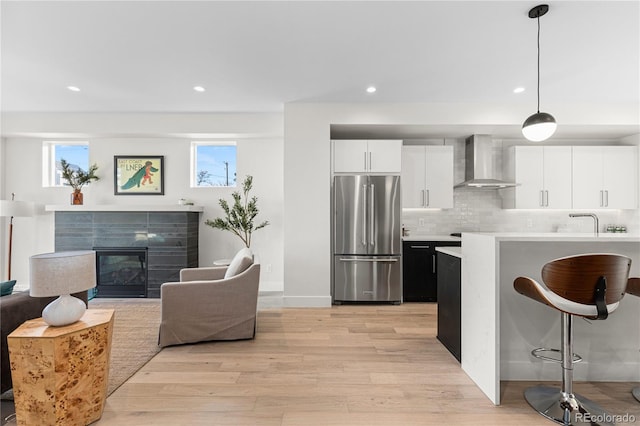 kitchen featuring light wood finished floors, a breakfast bar, high end refrigerator, wall chimney range hood, and tasteful backsplash