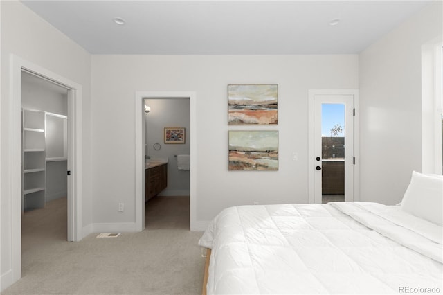 bedroom featuring visible vents, baseboards, ensuite bath, a walk in closet, and light colored carpet