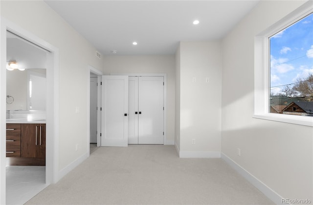 unfurnished bedroom with light carpet, recessed lighting, a closet, connected bathroom, and baseboards