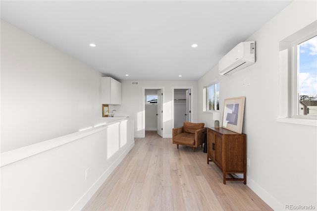 corridor featuring a wall unit AC, light wood-style flooring, a healthy amount of sunlight, and baseboards