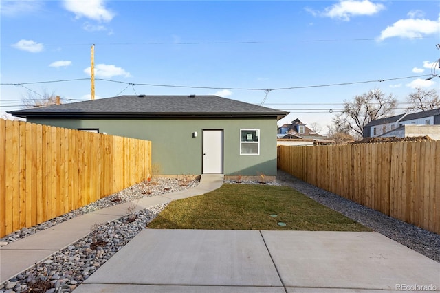 rear view of house featuring a yard, stucco siding, a shingled roof, and a fenced backyard