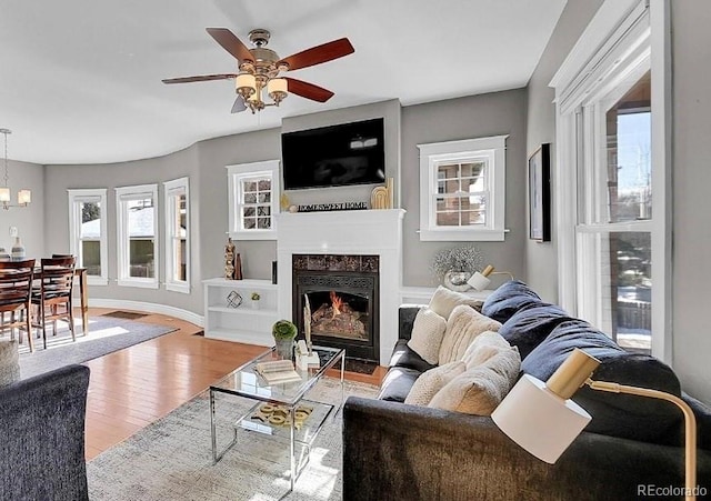 living room featuring a high end fireplace, ceiling fan with notable chandelier, and light hardwood / wood-style floors