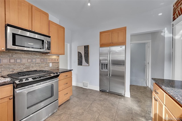 kitchen featuring tasteful backsplash, dark stone counters, light tile patterned floors, stainless steel appliances, and light brown cabinets