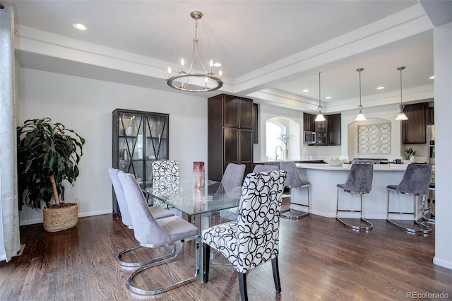 dining room featuring a tray ceiling, sink, dark wood-type flooring, and a notable chandelier