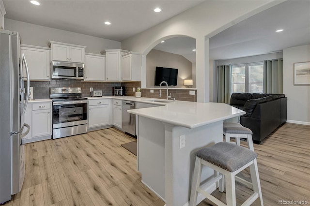 kitchen featuring white cabinets, kitchen peninsula, a breakfast bar area, stainless steel appliances, and light hardwood / wood-style flooring