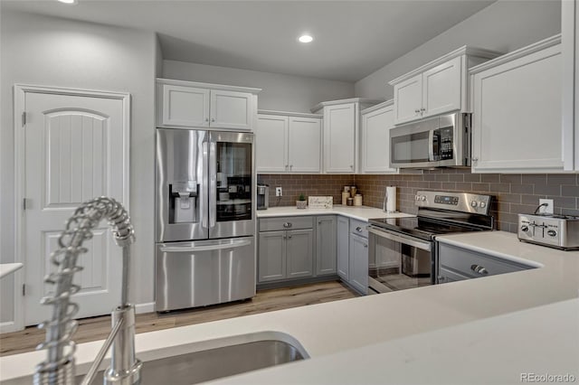 kitchen with white cabinets, appliances with stainless steel finishes, decorative backsplash, and light hardwood / wood-style flooring