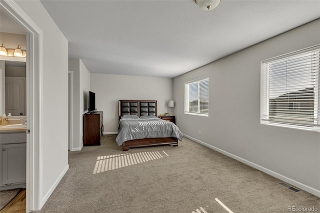 bedroom featuring light carpet, ensuite bath, and sink