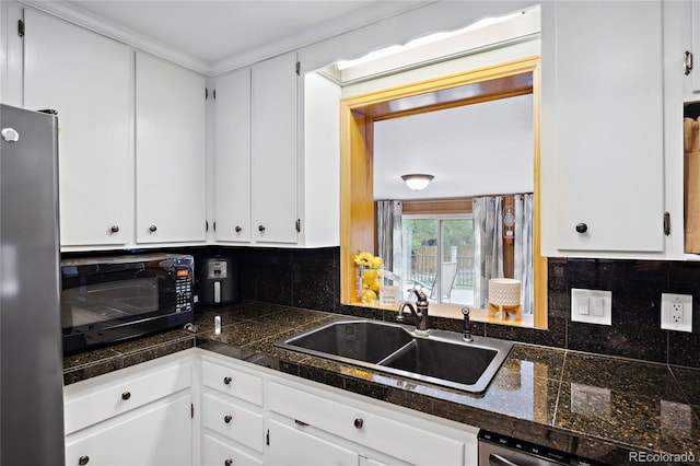 kitchen featuring black microwave, tile countertops, freestanding refrigerator, a sink, and white cabinetry