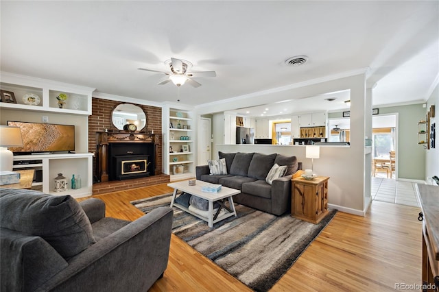 living room with crown molding, light wood-style floors, a ceiling fan, a fireplace, and baseboards