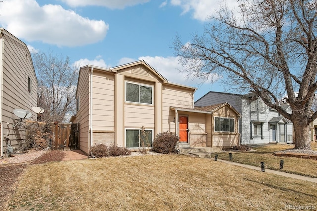 split level home featuring brick siding, fence, and a front lawn