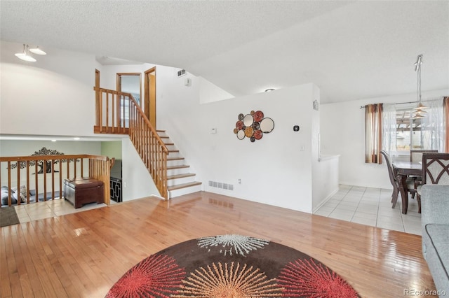 living area featuring lofted ceiling, visible vents, a textured ceiling, hardwood / wood-style floors, and stairs