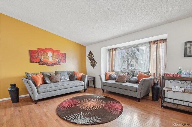 living area with lofted ceiling, a textured ceiling, hardwood / wood-style flooring, and baseboards