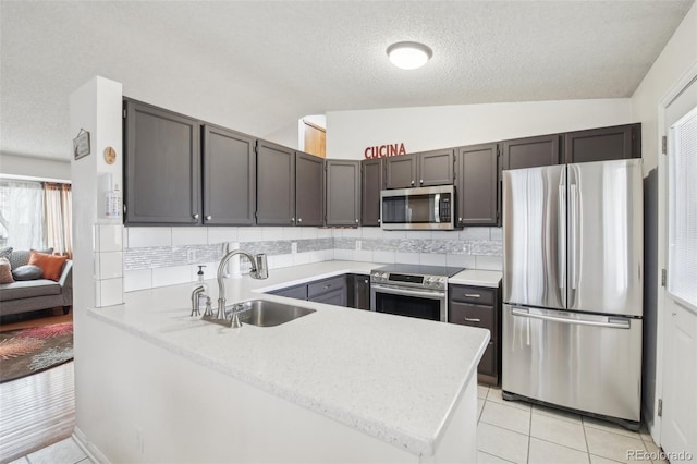 kitchen featuring light tile patterned floors, lofted ceiling, appliances with stainless steel finishes, a peninsula, and a sink