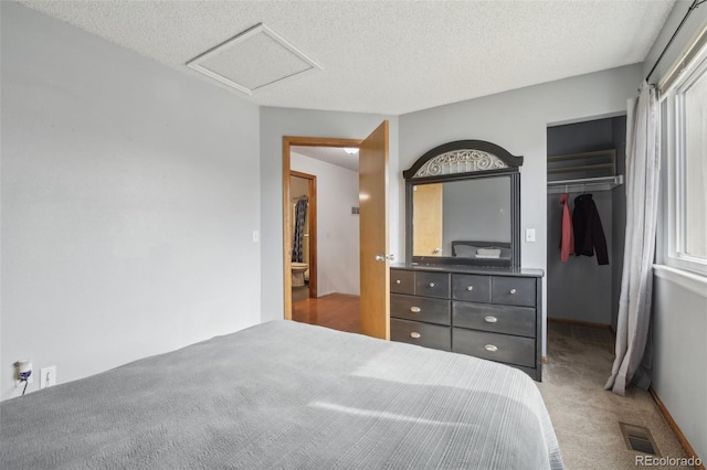 carpeted bedroom featuring a walk in closet, a closet, visible vents, attic access, and a textured ceiling