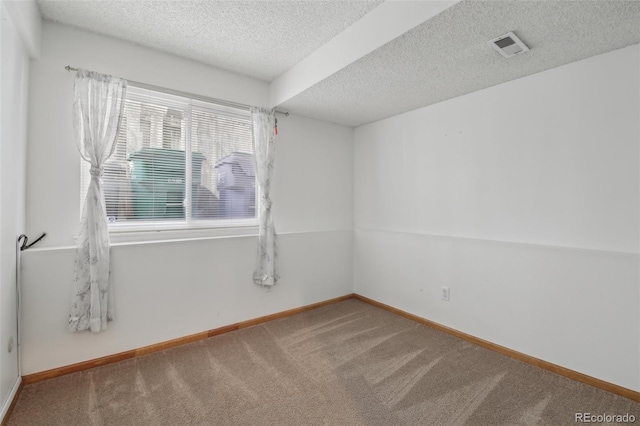 spare room with carpet, visible vents, baseboards, and a textured ceiling