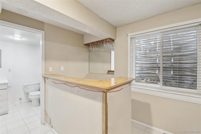 kitchen featuring baseboards, wooden counters, a textured ceiling, and light tile patterned flooring