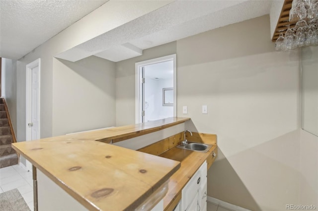 interior space featuring a textured ceiling, light tile patterned floors, a sink, and baseboards