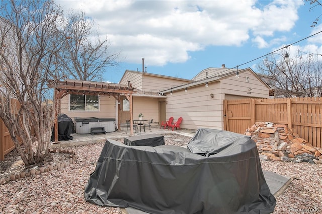 back of house with a hot tub, a pergola, a fenced backyard, and a patio