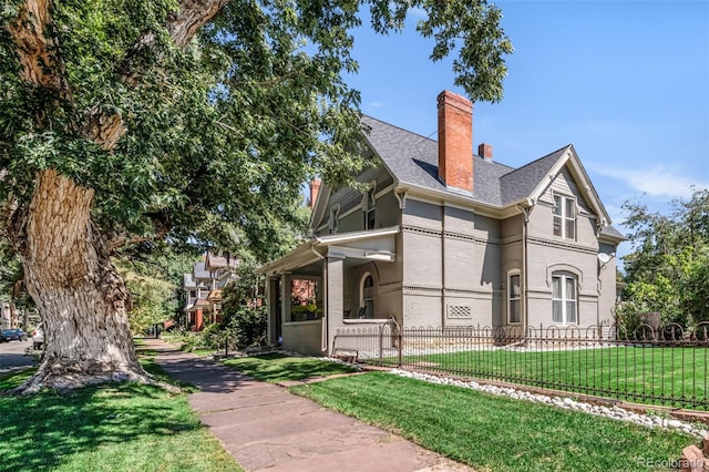 view of front of home featuring roof with shingles, fence, a chimney, and a front lawn