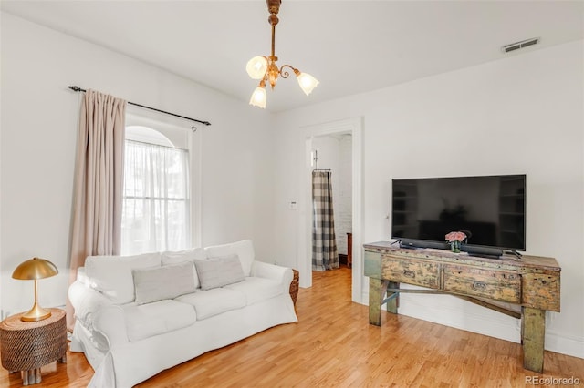 living room with wood finished floors, visible vents, and a notable chandelier