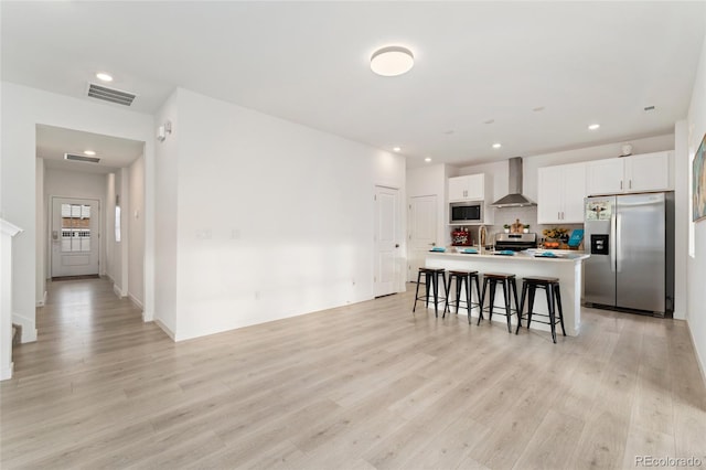 kitchen featuring a breakfast bar area, visible vents, appliances with stainless steel finishes, light wood-type flooring, and wall chimney exhaust hood