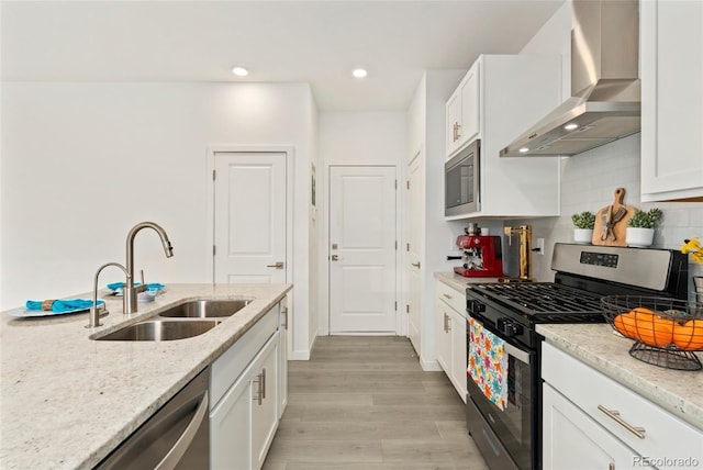 kitchen featuring stainless steel appliances, a sink, white cabinets, wall chimney range hood, and tasteful backsplash