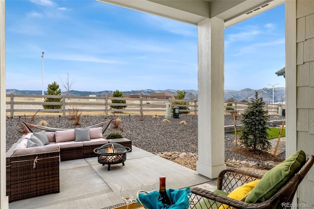 view of patio / terrace featuring fence, a mountain view, and an outdoor living space with a fire pit