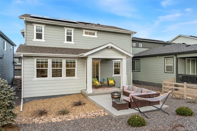 rear view of house with solar panels, a shingled roof, a patio area, and an outdoor living space with a fire pit