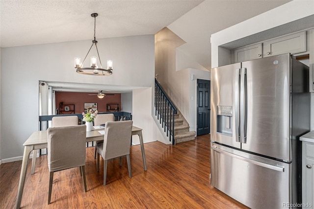 dining space with ceiling fan with notable chandelier, wood finished floors, baseboards, vaulted ceiling, and stairway