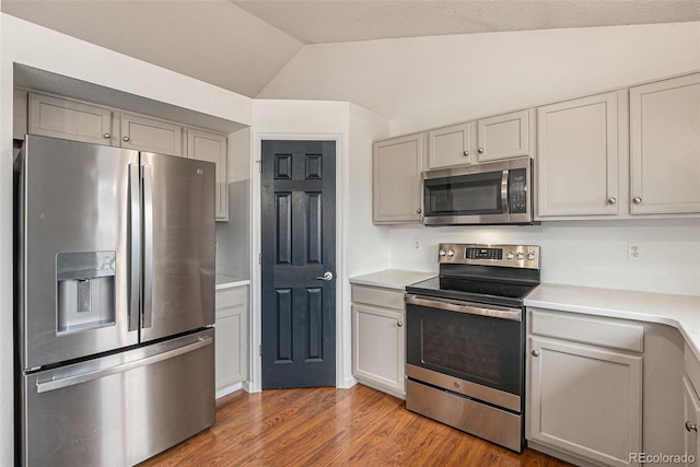 kitchen with appliances with stainless steel finishes, wood finished floors, vaulted ceiling, light countertops, and gray cabinetry