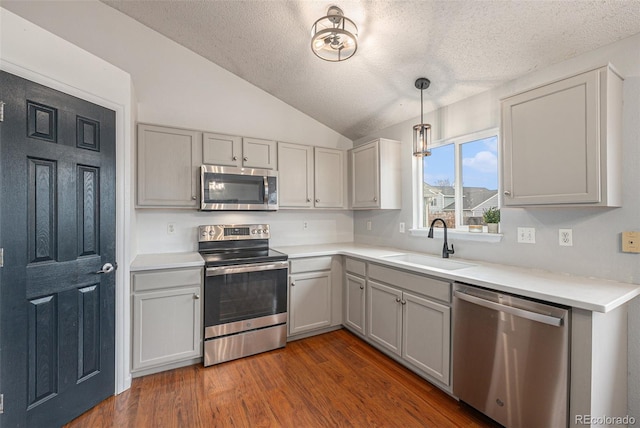 kitchen with appliances with stainless steel finishes, wood finished floors, light countertops, vaulted ceiling, and a sink