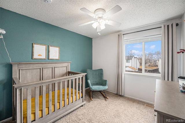 bedroom with a textured ceiling, carpet floors, a ceiling fan, baseboards, and a nursery area